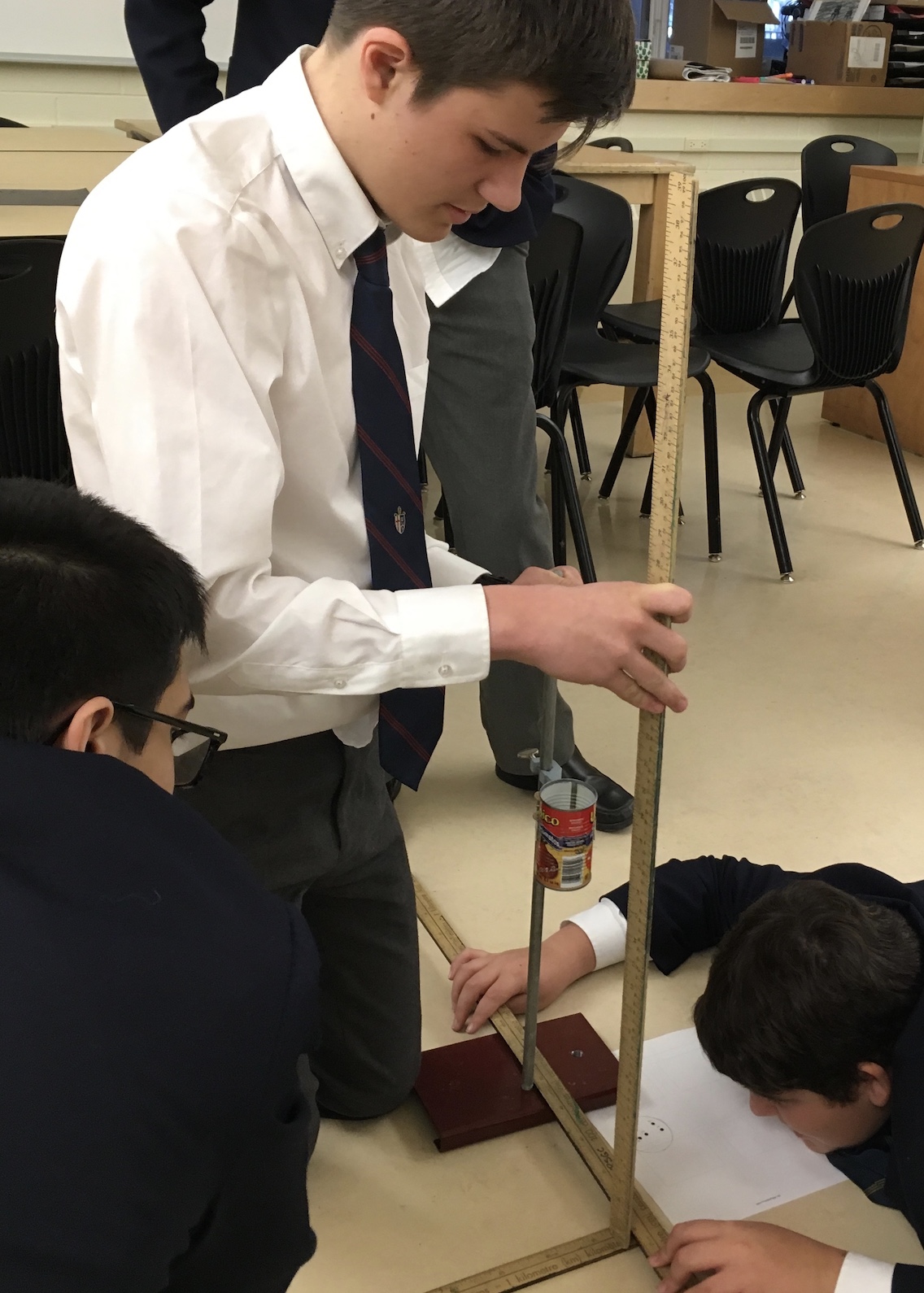 Students measure the height of the tomato paste can that is attached to a lab or retort stand.